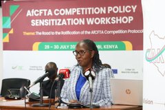 A woman in glasses and a checkered blazer speaks at a podium during the AfCFTA Competition Policy Sensitization Workshop in Kenya, 29-30 July.