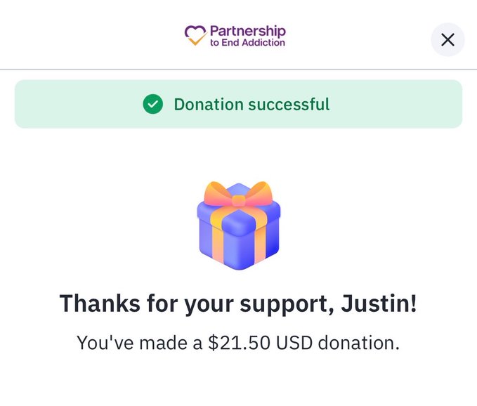 A donation confirmation screen from Partnership to End Addiction showing a successful $21.50 USD donation by Justin, celebrating a first contribution to the cause of addressing addiction. The gift box graphic and thank-you message reinforce the post's message that "addiction doesn't discriminate," marking a meaningful first step in supporting those affected.