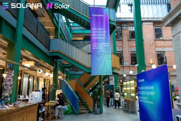 Banners for the "Solar Hackathon" and "Solana" are displayed in an industrial-style event space with green beams, where attendees gather near booths, reflecting the Shanghai hackathon event mentioned in the post.