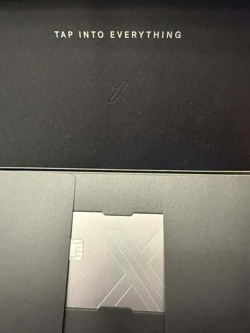 A dark gray promotional box or packaging with the text 'TAP INTO EVERYTHING' and an embossed 'X' logo, containing a metallic card with an 'X' design.