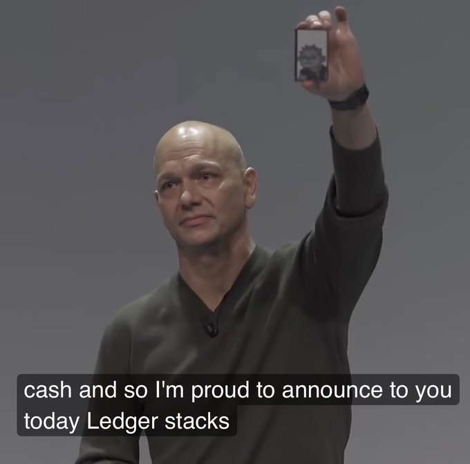 Bald man holding up a Ledger hardware wallet displaying a pixel art image, with the caption: 'cash and so I'm proud to announce to you today Ledger stacks'.
