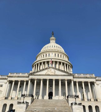 A photograph of the United States Capitol building with its iconic white dome and columns under a clear blue sky.