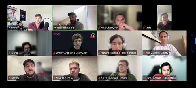 The image shows a group of people sitting around a table for an online meeting or conference call using a video conferencing platform like Zoom. There are at least 13 people visible in the image, with some appearing closer to the camera while others are further away. They seem to be engaged in a discussion or presentation, possibly related to the topic of "Phone Salesman of the Year". The background of the image is black and white, which contrasts with the colorful faces of the participants.