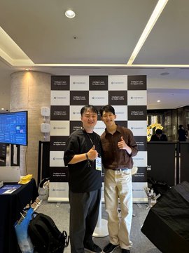 Two men smile and give thumbs-up while posing in front of a backdrop with "TokenPost" and "KBW" logos. The image captures the moment after TokenPost's interview with the CTO at Korea Blockchain Week, discussing Newton and tokenized finance.