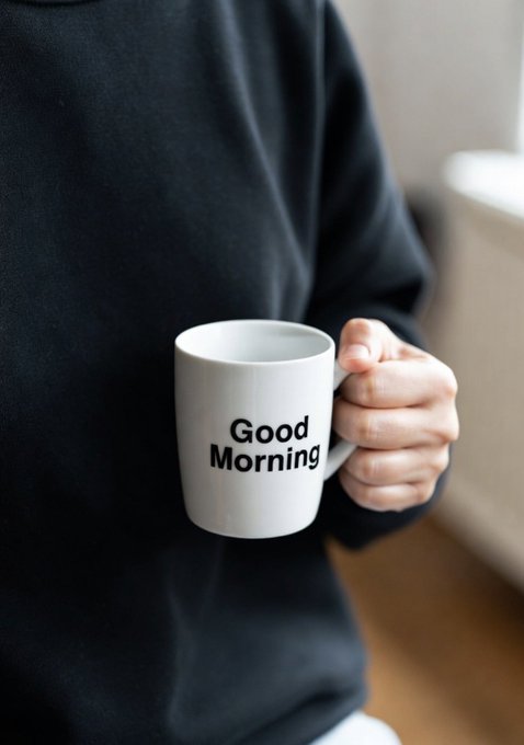 A person in a black sweatshirt holding a white ceramic mug that reads 'Good Morning' in black text.