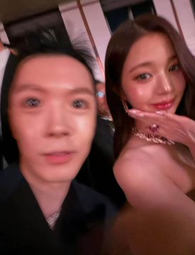 The image features two people, a man with black hair and a woman with brown hair, standing next to each other. They are both wearing dark clothing, which complements their serious expressions as they pose for the camera. The background of the photo is blurred, drawing attention to the subjects in focus. The caption "我真的不行了 这个开心到模糊的世纪照片竟然要花400万" suggests that they are at a formal event or gathering, possibly a party.