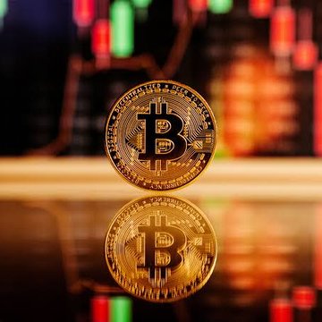 A physical gold Bitcoin token stands upright on a reflective surface with its mirrored image below, set against a blurred backdrop of red and green financial trading charts. The coin prominently displays the iconic "B" Bitcoin symbol, visually reinforcing the post's message about Bitcoin's strong September performance and emerging dominance in the market.