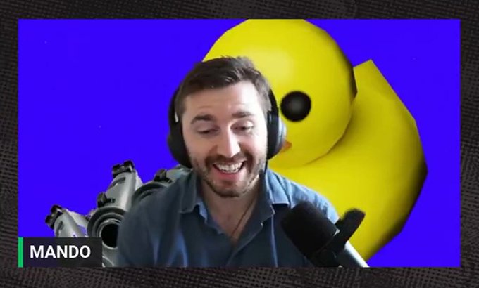 A man wearing headphones labeled "MANDO" smiles while speaking into a microphone, with a large yellow emoji face in the background against a purple backdrop. The image relates to the post as it features Mando (likely @rektmando), the crypto influencer mentioned, whose background and story are being analyzed in connection to the $EPIK token and educkcoin.