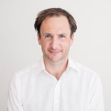 A headshot of a man with short brown hair and light stubble, wearing a white button-up shirt and smiling slightly against a plain light background. The image likely depicts Richard Heathcote, Tether's former CIO, who is reportedly seeking buyers for part of his 1.26% stake in the company.