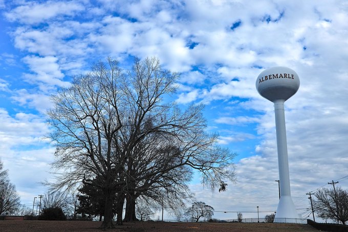 A tall white water tower labeled 'ALBEMARLE' stands beside a large bare tree under a partly cloudy sky.