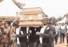The image shows a group of people dressed in suits, carrying a large wooden casket with a bird perched on top. They are walking down a street or path, possibly participating in an event or procession. The presence of the bird on the casket suggests that they might be honoring someone or commemorating a significant occasion related to death and mourning.