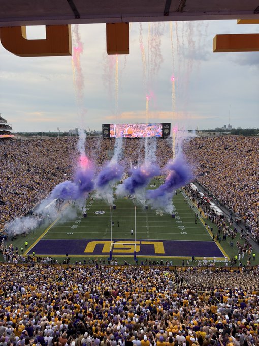 Purple smoke rises over the field at Tiger Stadium as the LSU Tigers emerge from the tunnel, with "LSU" boldly painted in the end zone and the SEC logo visible on the turf — a quintessential SEC football atmosphere perfect for any college football enjoyer.