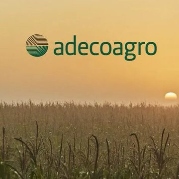 The image features an advertisement for a Bitcoin mining facility that uses sugarcane waste as its primary source of energy. The setting appears to be a field filled with tall corn plants at sunset, creating a serene atmosphere. The text on the image reads "Adecoaagro" and "TETHER-BACKED FIRM TO MINE BITCOIN USING SUGARCANE WASTE Adecoagro is set to launch a Bitcoin mining facility in Brazil powered by electricity generated from leftover sugarcane material".