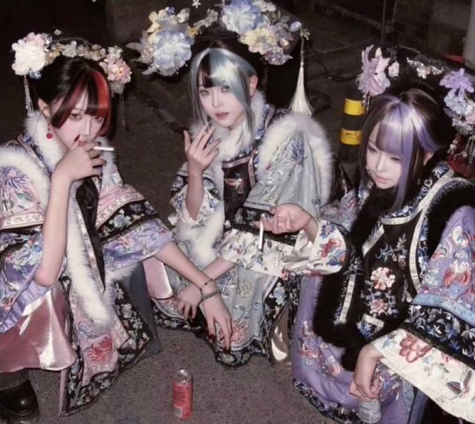 Three young women dressed in elaborate Japanese-style kimonos and floral hair ornaments, posing together at night with a red Coca-Cola can on the ground in front of them.