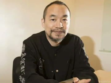 The image shows Machi Big Brother, the NFT collector referenced in the post, smiling while wearing a black jacket. The caption accompanies news of his significant loss selling Bored Ape #5670 for only 9 ETH, far below his original 85 ETH purchase price five years earlier.