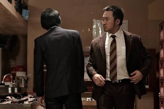 Two men in business suits stand in a dimly lit, cluttered room—one facing away in a dark suit while the other, in a brown suit and striped tie, appears to be negotiating or confronting him. The tense exchange visually mirrors the post's theme of a behind-the-scenes power struggle over the "reserve interest" split between OUSD and Circle/USDC, suggesting a private deal rather than a public market battle.