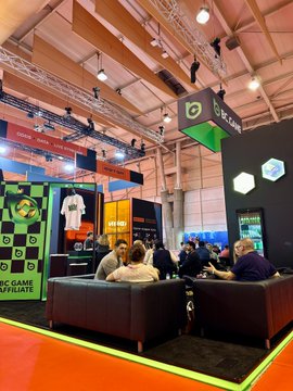 An Optibet expo booth at a trade show with black and green branding, where staff in black shirts assist visitors on dark sofas, with promotional screens showing an 'Epic game affiliate' offer.