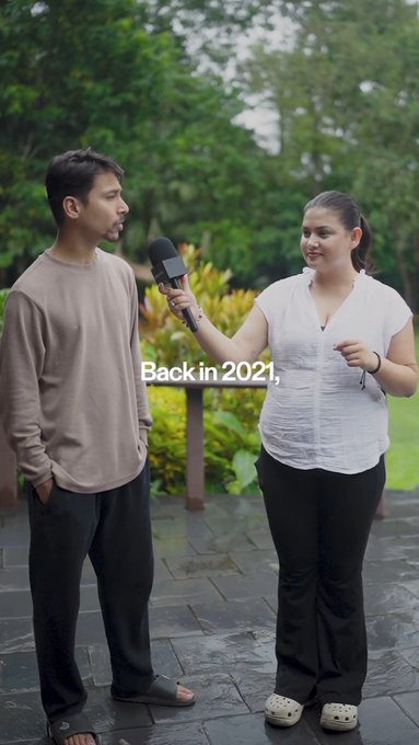A woman holds a microphone interviewing a man outdoors, with the subtitle 'Back in 2021,' displayed on screen.
