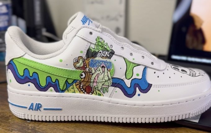 A custom hand-painted white Nike Air Force 1 sneaker featuring Rugrats characters and dripping green, purple, and blue paint designs.