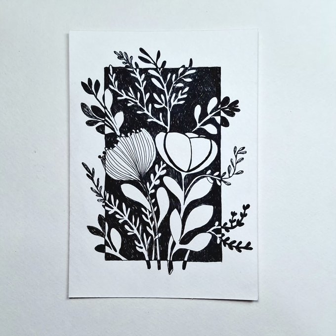 A black and white printed artwork features intricate floral and leaf designs carved into a rectangular black block, surrounded by white botanical illustrations on a plain white surface.