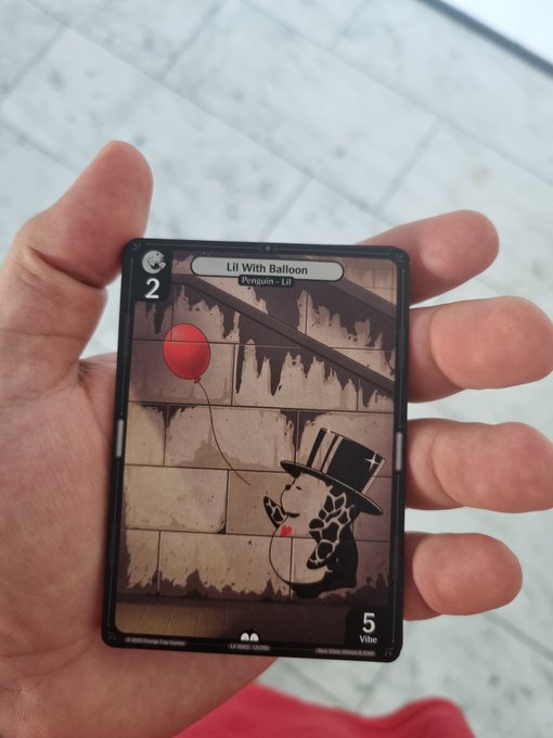 A hand holds a trading card titled 'Lil With Balloon' featuring a character in a top hat holding a red balloon, with stats showing 2 and 5 Vibe.