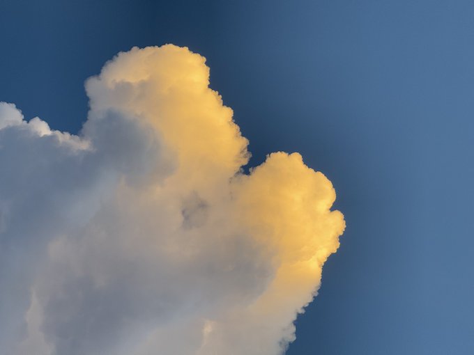 A large white cloud is illuminated with golden light against a deep blue sky.