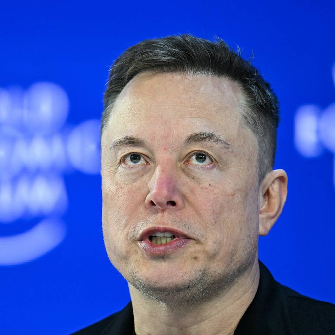 Elon Musk speaks against a blue backdrop, pictured in the accompanying article warning that America will "1000% go bankrupt and fail as a country," with a link to thestreet.com/crypto/markets.