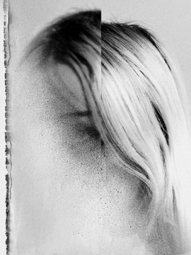 An artistic, grainy black-and-white image depicts a person with their head bowed, their long hair obscuring their face.
