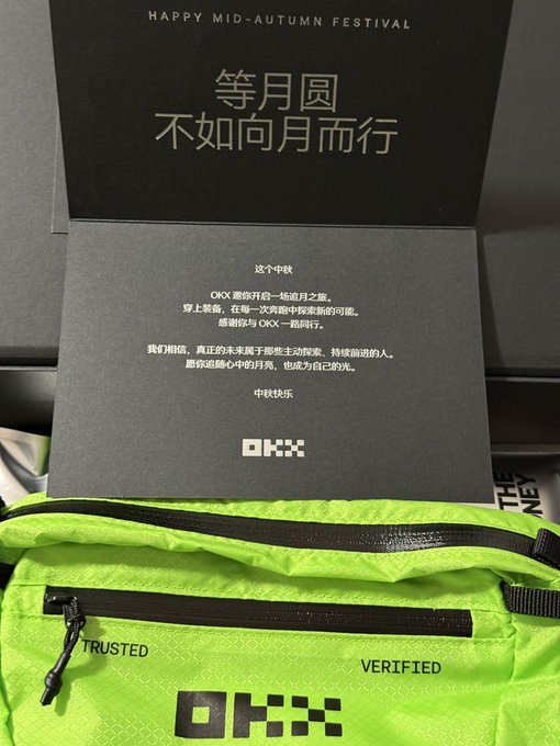 OKX Mid-Autumn Festival gift box containing a neon green bag with 'TRUSTED VERIFIED' text and OKX branding, alongside a card with Chinese text wishing '等月圆,不如向月而行'.