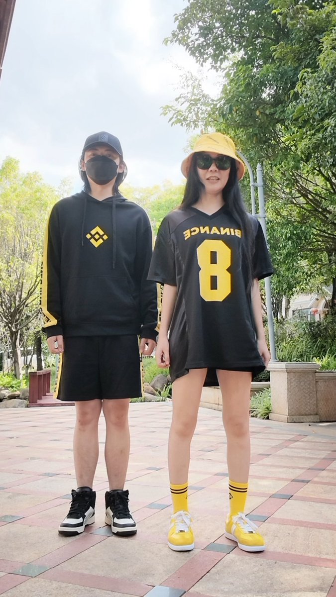 Two friends pose outdoors coordinating in black and yellow streetwear, with the girl wearing a jersey displaying "BINANCE" and the number "8" alongside bright yellow sneakers and matching socks, promoting Binance-branded shoes as referenced in the post about practicing the "Flash Step."