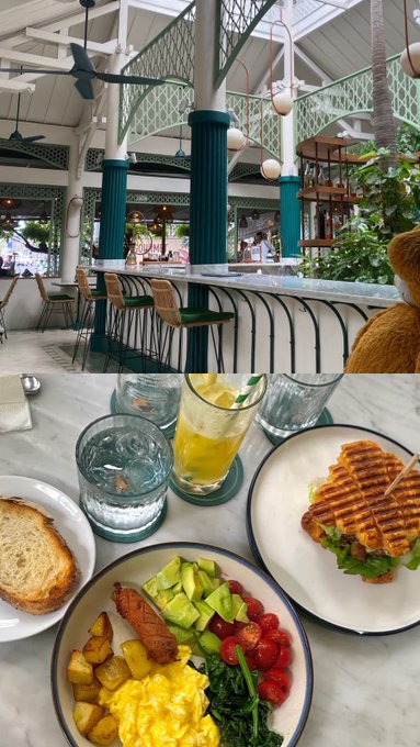 The image shows a colorful brunch spread featuring scrambled eggs, potatoes, avocado, waffles, and a refreshing drink at a tropical-style restaurant with green columns and ceiling fans, perfectly complementing a cheerful "Gm fam" morning greeting.