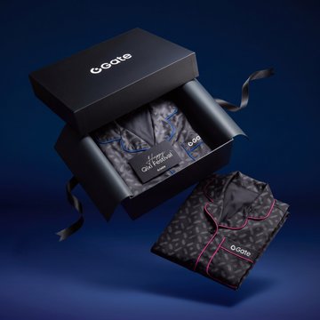 A luxury product packaging featuring a black gift box branded 'GGate' containing patterned silk pajamas and a robe with 'Keep Your Future' tags, displayed on a dark blue background.
