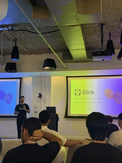 A presenter pitches Blink to an audience at Nitro Demo Day, with a slide reading "Blink - One tap deposits for the next generation of consumer apps" visible on the projector screen behind him.