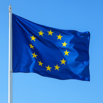 The European Union flag waves against a blue sky, symbolizing the regulatory body scrutinizing cryptocurrency exchange Binance for allegedly circumventing a wind-down order by using a legal exemption to continue serving EU customers without proper licensing.