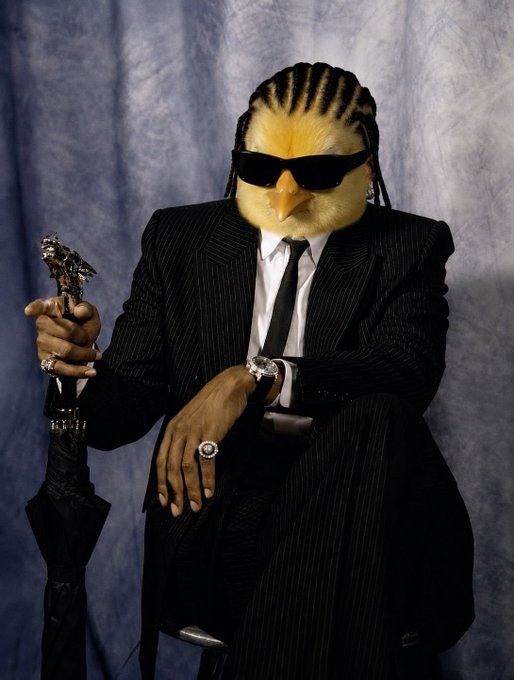 A person wearing a pinstripe suit, black tie, and sunglasses, with a yellow bird/chicken mask covering their face, holding an umbrella and wearing multiple rings.