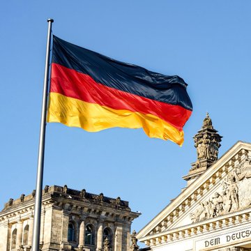 A German flag flies prominently against a clear blue sky above the Reichstag building, with the visible inscription "DEM DEUTS..." referencing the German national motto, symbolizing the government now considering a 25% tax on crypto profits regardless of holding period. The image underscores Germany's shifting stance on cryptocurrency taxation, moving from its current tax-free treatment for assets held over a year to a flat 25% levy on all crypto gains.