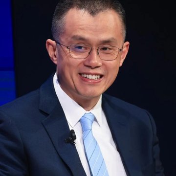 A portrait of a smiling middle-aged man with glasses, wearing a navy suit and light blue tie.