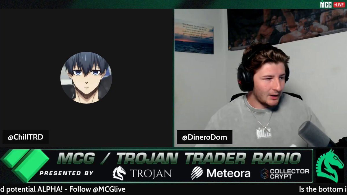 The image shows two people sitting behind microphones, with one person wearing headphones and looking at the other person who has their face displayed on a computer screen. The person on the screen appears to be a character from an anime or video game, while the individual in the background is likely the host of the show or event they are participating in.