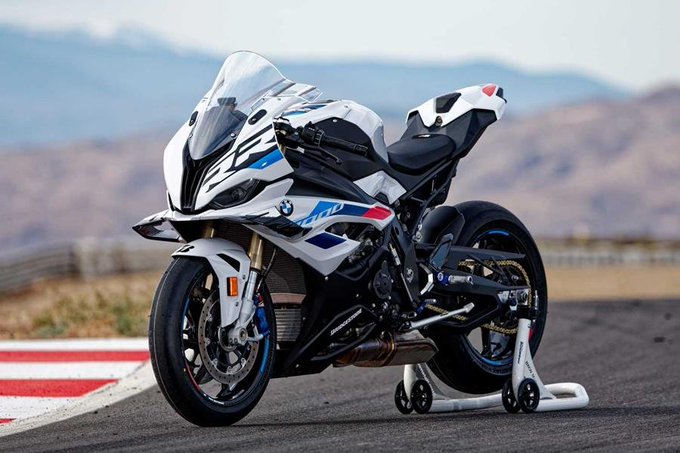 A white, black, and blue BMW HP4 sport motorcycle parked on a track with mountains in the background.