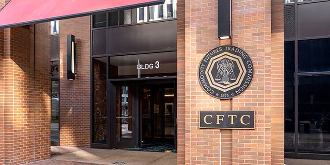 The exterior entrance of a brick building displays signs reading 'BLDG 3', 'CFTC', and 'COMMODITY FUTURES TRADING COMMISSION' along with the agency's seal.