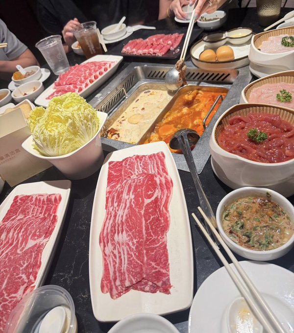 A hot pot feast featuring marbled beef slices, napa cabbage, a split spicy and mild broth, and various dipping dishes is laid out at Haidilao, as the caption celebrates it as a perfect start to Token2049 Singapore week with Mask Network hosts.