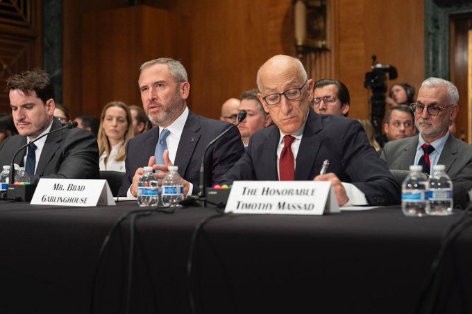 A Senate hearing showing several men seated at a witness table, with nameplates identifying 'Mr. Brad Garlinghouse' and 'The Honorable Timothy Massad' among those testifying.