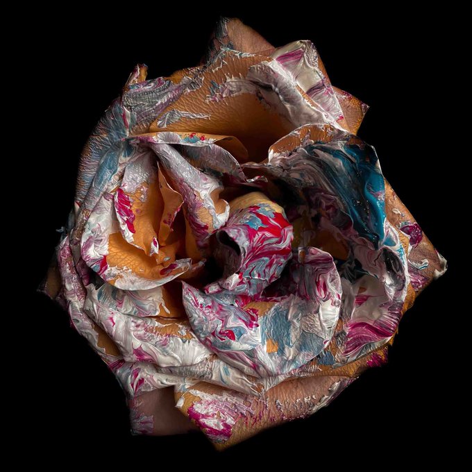 A close-up photograph of a sculpted, textured rose made from a swirled mix of pink, blue, white, and metallic materials against a black background.