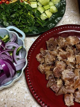 A top-down view of food ingredients prepared for cooking: chopped meat on a dark red plate, sliced red onions in a white bowl, and fresh herbs and diced cucumbers on a green plate.