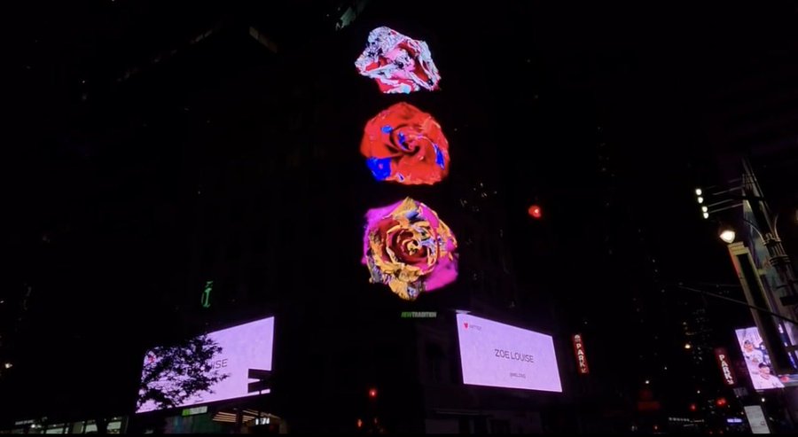 A nighttime city scene featuring a building displaying colorful rose-shaped digital art projections stacked vertically, with illuminated billboards showing 'ZOE LOUSE' below.
