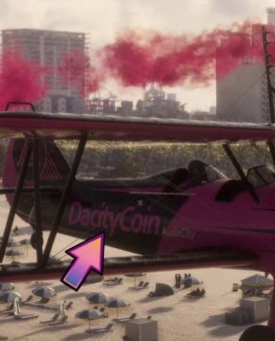 A pink advertising aircraft or vehicle marked “DacityCoin” with red smoke trails, highlighted by a large arrow, at what appears to be a beachside event.