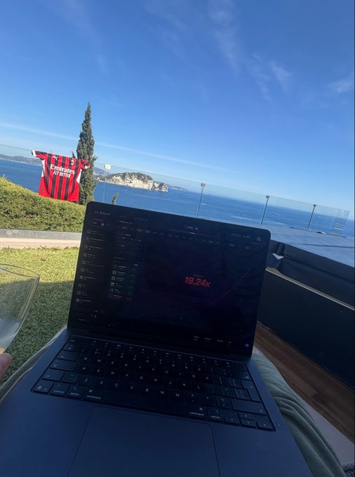 A laptop displaying charts and a '18.24%' figure sits on a table at an outdoor cafe, with an Emirates flag and the ocean visible in the background.