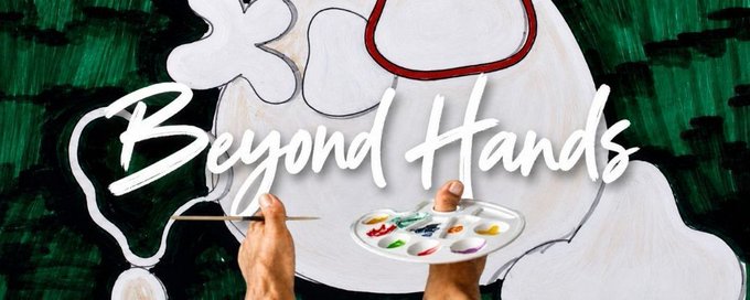 A close-up shot of hands holding a paintbrush and a palette with colorful paints in front of a green textured background, with the white text 'Beyond Hands' overlaid in script.