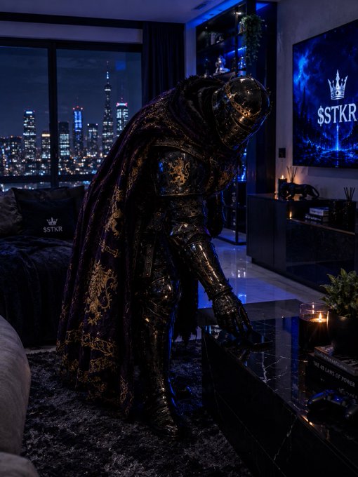 A figure in full dark knight armor with a decorative purple and gold cape stands in a modern apartment with a city skyline view at night, next to a TV screen displaying '$STKR' branding.