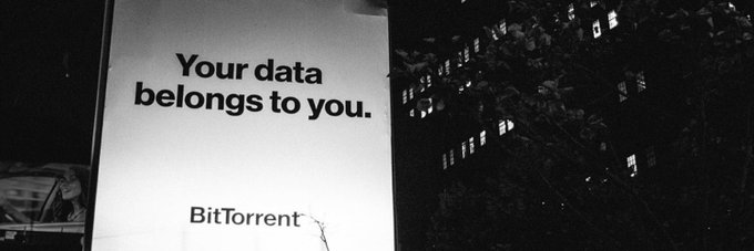 Black and white photograph of an illuminated billboard at night displaying 'Your data belongs to you.' with the BitTorrent logo below.